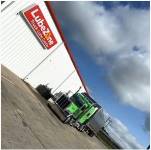 A green semi-truck parked by a LubeZone Truck Lube Center on a cloudy day