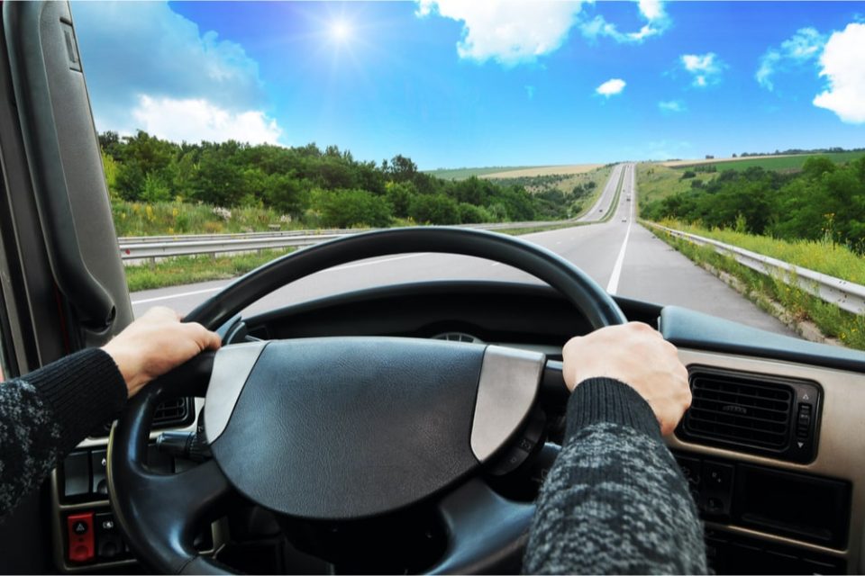 View out the front windshield of a semi-truck, highway and blue sky ahead.