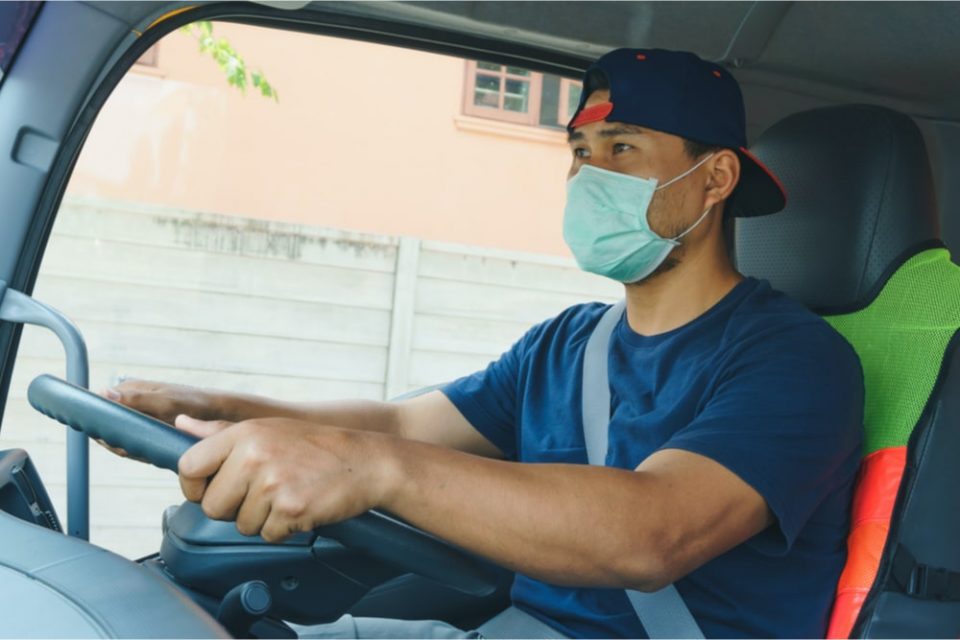 Truck driver sitting in driver's seat of semi wearing a mask.