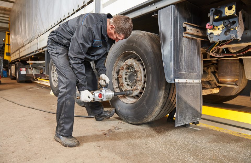 male mechanic in coveralls removing lug nuts from a semi-truck