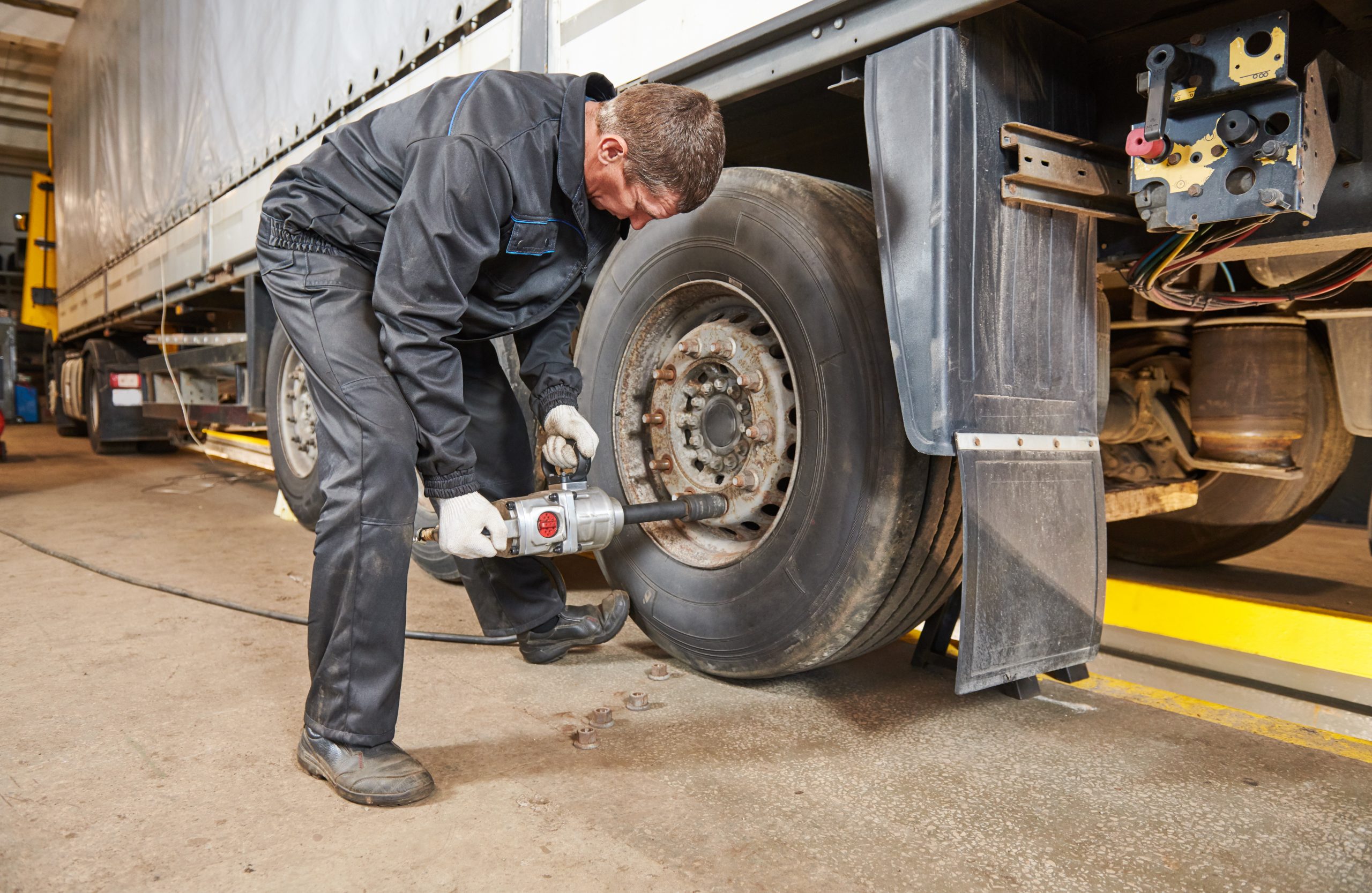 male mechanic in coveralls removing lug nuts from a semi-truck