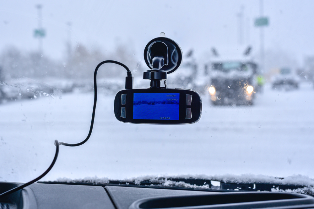 Image of a truck dash cam stuck to the inside of a windshield. Snow and rainy conditions outside.