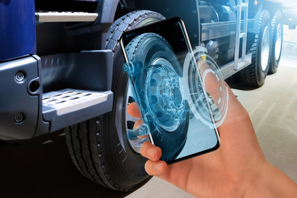 Hand holding up a phone near a semi-truck.