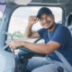 Male trucker in the cab of a truck facing the camera and tipping his baseball cap.