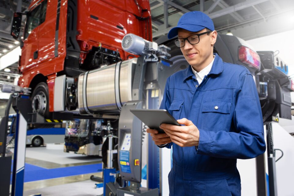 Mechanic in coveralls standing in front of semi-truck on lift.