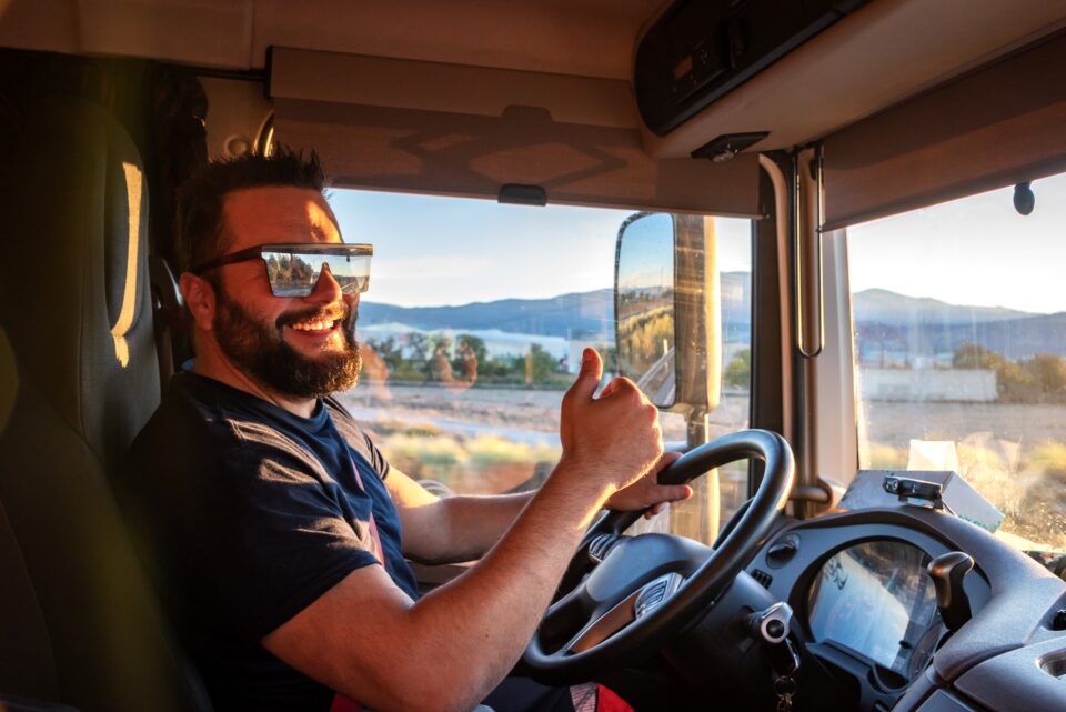Man wearing sunglasses and a beard giving a thumb's up in the cab of a truck.