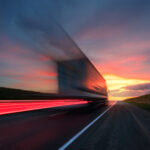Blurred exposure of a semi-truck speeding away toward the sunset.