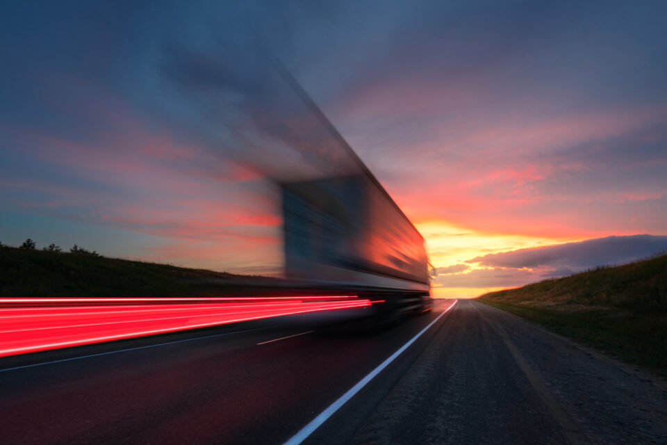 Blurred exposure of a semi-truck speeding away toward the sunset.