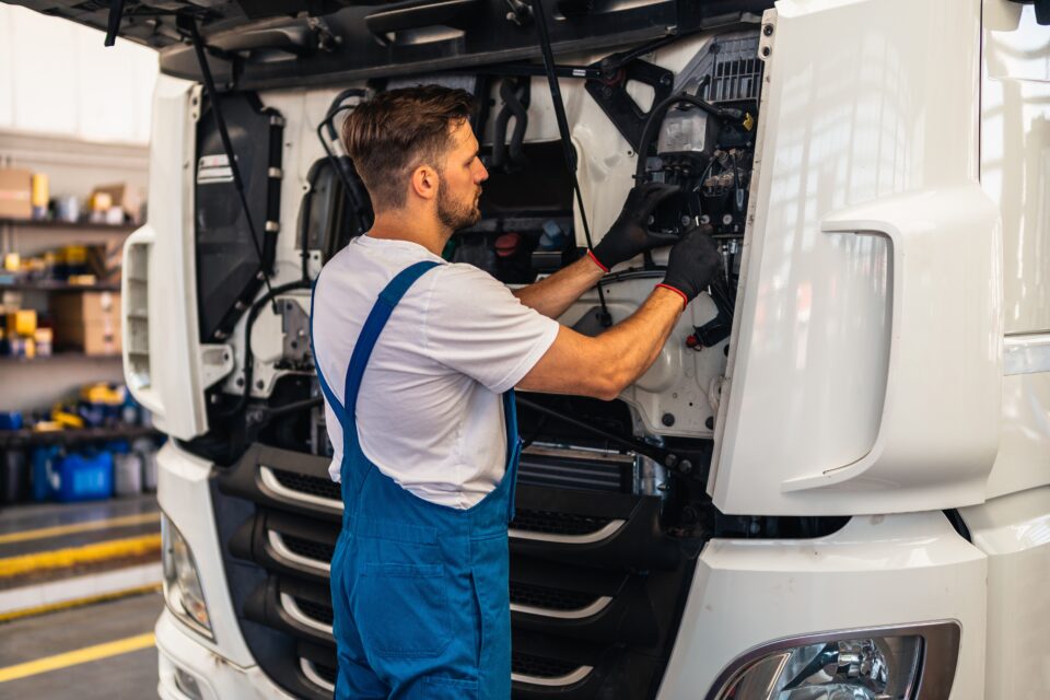 Bearded man in overalls working on a semitruck.