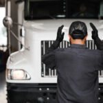 A mechanic stands in front of a white semi-truck.
