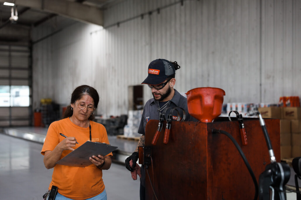 two workers review a clipboard beside industrial equipment