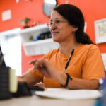Woman in an orange shirt smiling while using a computer at a desk