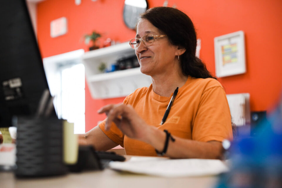 Woman in an orange shirt smiling while using a computer at a desk